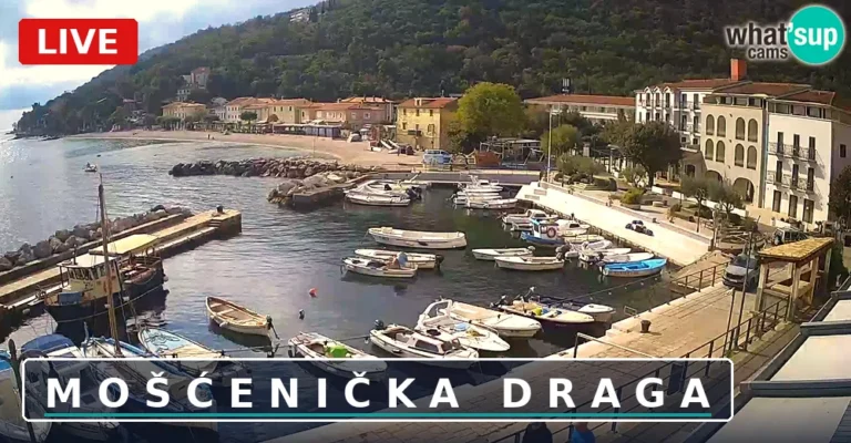 Pogled spletne kamere v živo na pristan v Mošćenički Dragi z ribiškimi čolni in plažo v ozadju, Hrvaška